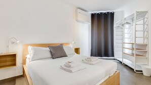 A neatly made bed with white linens, a wooden headboard, and a grey pillow. There is a white wardrobe with shelves and a white bucket on the floor. - BDC - The Left Loft in Trastevere (Roma)