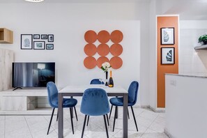 A modern dining area with a white table, blue chairs, a TV, and artwork on the walls.