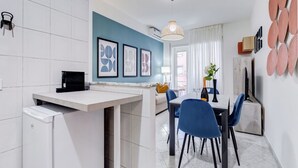 A modern kitchen with a dining area, white tiles, a blue accent wall, and a ceiling light fixture.