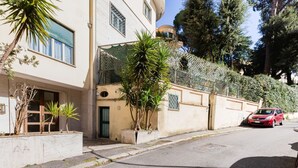 A residential street with a building featuring a balcony, a car parked on the street, and trees. - Classy Apartment | Auditorium & Villa Borghese (Roma)