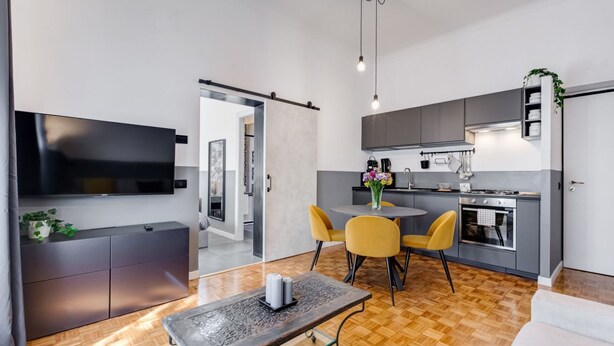 A modern kitchen with a dining area, a TV mounted on the wall, and a wooden floor. - Classy Apartment | Auditorium & Villa Borghese (Roma)