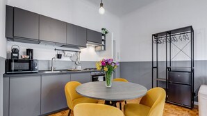 A modern kitchen with grey cabinets, a round table with yellow chairs, a black refrigerator, and a hanging clothes rack. - Classy Apartment | Auditorium & Villa Borghese (Roma)