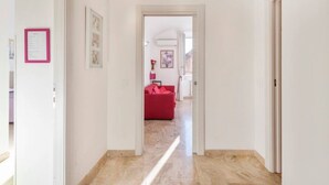 Un pasillo que conduce a una sala de estar con un sofá rojo, cuadros en las paredes y una puerta a la derecha.