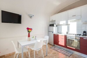 A compact kitchen with white cabinets, a microwave, a refrigerator, and a stove. There is a dining table with chairs and a vase of flowers.