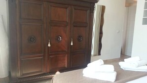 Un armario grande de madera con varias puertas, una cama con colcha marrón y una pila de toallas blancas sobre la cama.