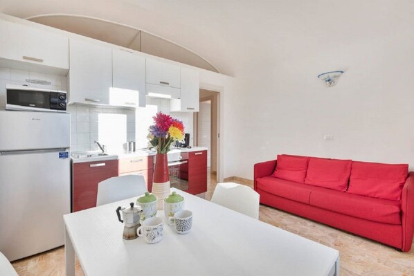 A modern kitchen with white cabinets, a red sofa, and a dining table with coffee cups.