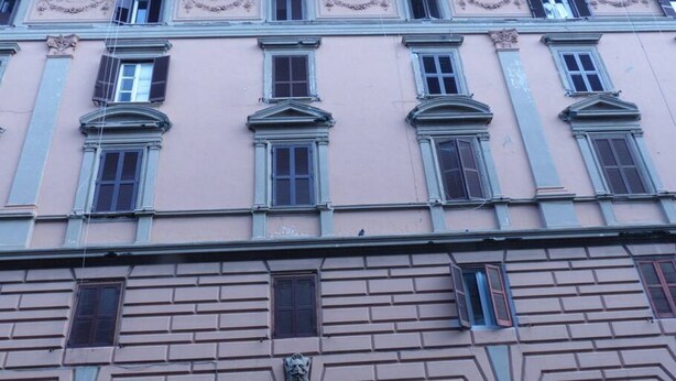 Fachada de edificio con varias ventanas, algunas con contraventanas, y un elemento decorativo de piedra en la base.