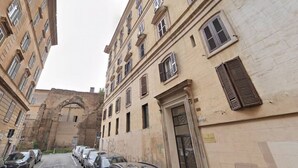 Une rue étroite, bordée de voitures garées, et un immeuble doté de nombreuses fenêtres et d’une porte.