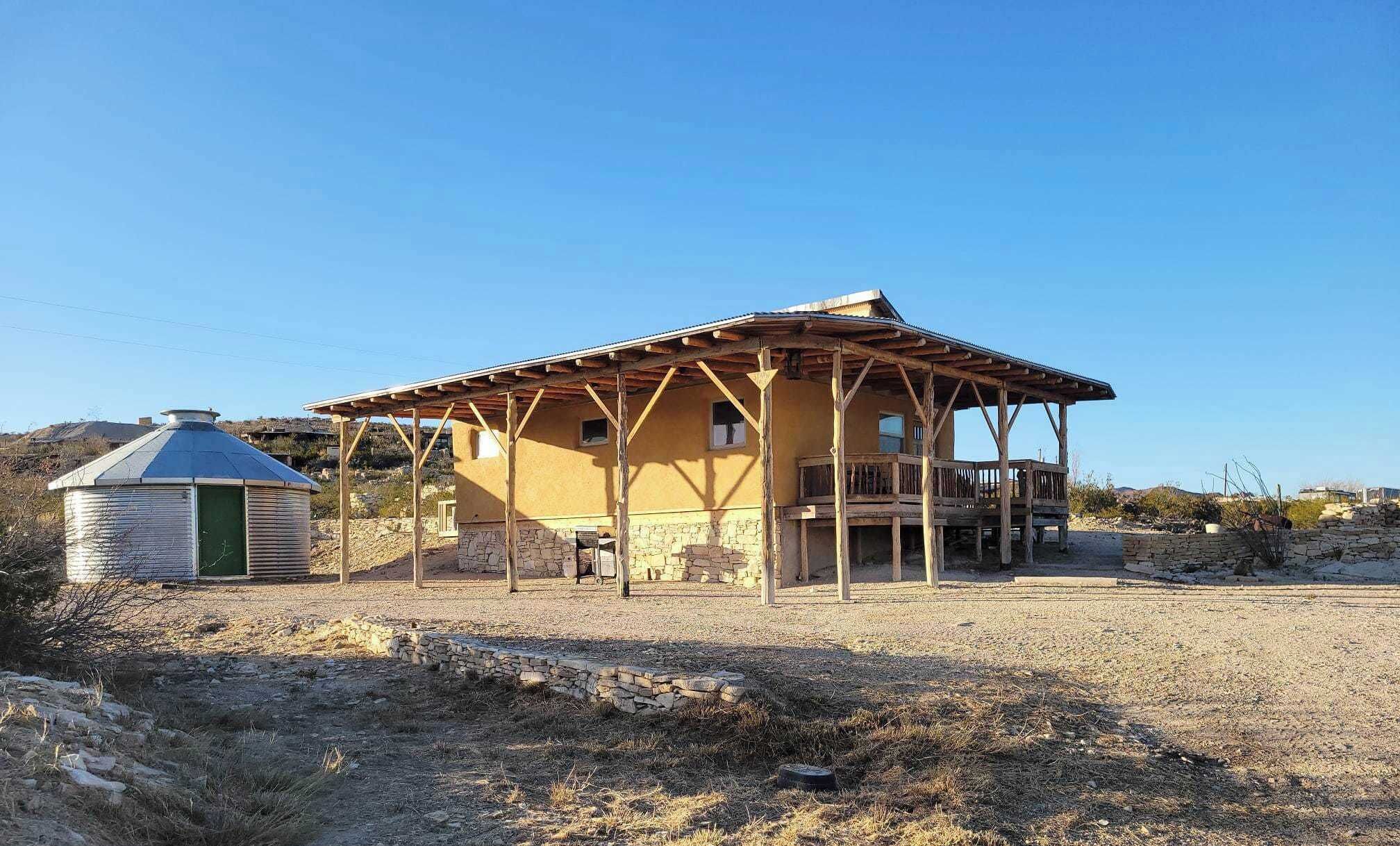 A rustic building with a wooden porch, a stone wall, and a silo.