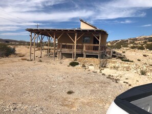 A rustic wooden cabin with a balcony, surrounded by a dry, rocky landscape.