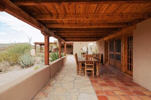 An outdoor patio with a wooden pergola, stone flooring, and a table set for dining.