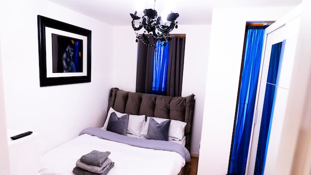 A bedroom with a bed, a chandelier, a framed picture on the wall, and blue curtains. - East London 1-bed Apt, Sleeps 2, With Parking (London)