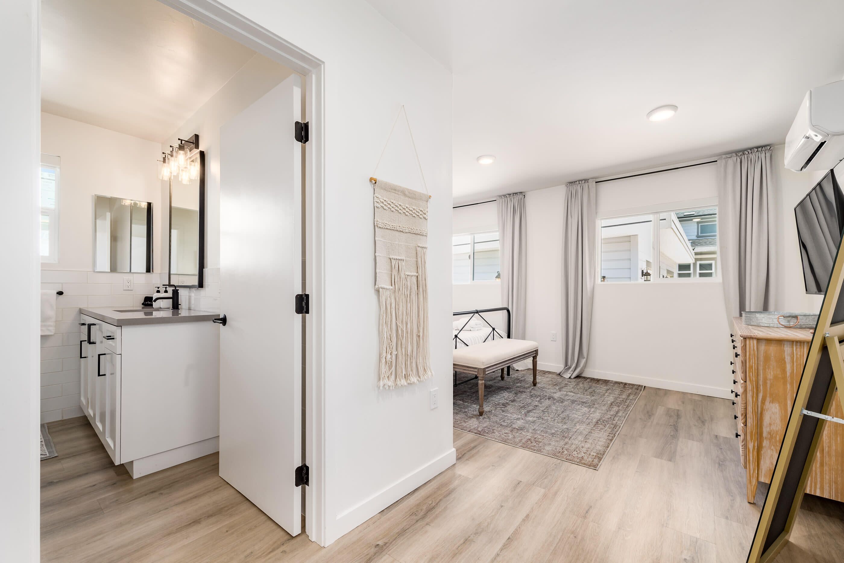 A modern, well-lit room with a kitchenette, a bed with a headboard, and a large window with curtains.