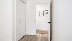 Ein Flur mit einer weißen Tür, einem Lichtschalter und einem gerahmten Bild an der Wand.