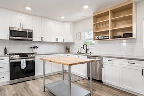 A modern kitchen with white cabinetry, stainless steel appliances, a wooden table, and a built-in wine rack. - New Midtown Farmhouse - Hot Tub, Patio, Gym (Santa Cruz)