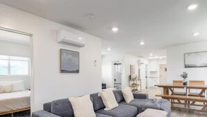 A modern living room with a grey sofa, a dining table, and a kitchen in the background.