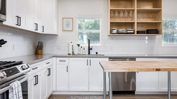 A modern kitchen with white cabinetry, a stainless steel range hood, a built-in dishwasher, and a wooden table.