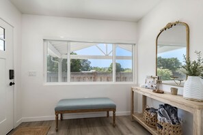 A room with a bench, a large window, a mirror, and a console table with a vase and a magazine. - New Midtown Farmhouse - Hot Tub, Patio, Gym (Santa Cruz)