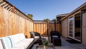 A patio with a wooden fence, wicker furniture, and a sliding glass door leading to an interior space. - Pleasure Point Getaway with hot tub, dog friendly! (Santa Cruz)