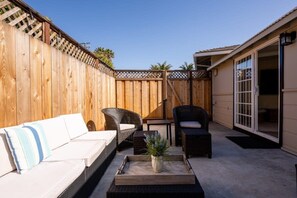 Eine Terrasse mit Holzzaun, Korbmöbeln und einer Glastür, die zu einem Innenbereich führt.