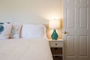 Un lit avec du linge de lit blanc, une lampe turquoise sur une table de chevet et une porte fermée.