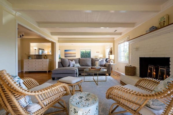 A living room with a fireplace, sofas, and wicker chairs. - Pleasure Point Getaway with hot tub, dog friendly! (Santa Cruz)