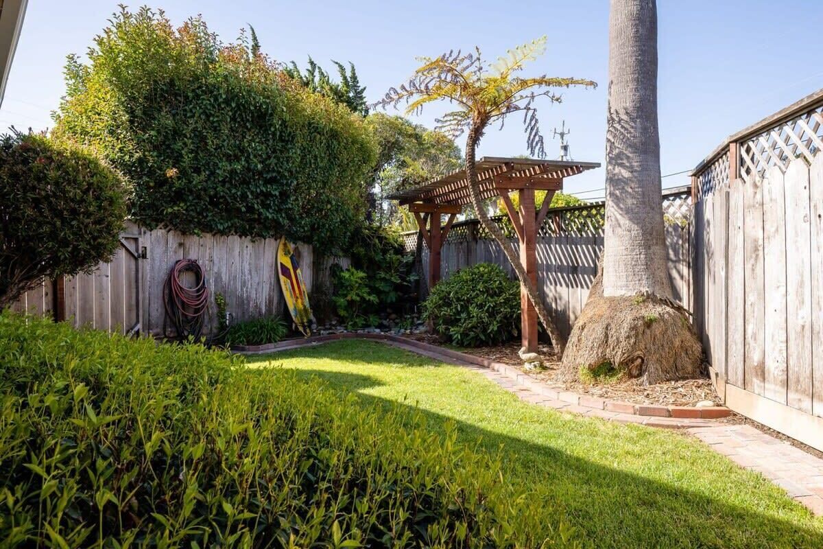 Um jardim bem cuidado com uma pérgola de madeira, uma palmeira e uma cerca de madeira.