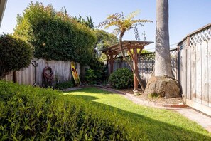 A well-maintained garden with a wooden pergola, a palm tree, and a wooden fence. - Pleasure Point Getaway with hot tub, dog friendly! (Santa Cruz)