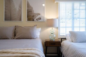 Un dormitorio con una cama, una mesita de noche con lámpara y una ventana con persianas.