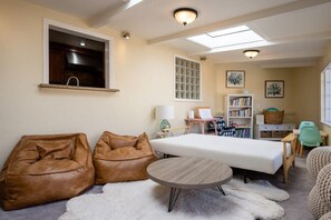 Una habitación acogedora con una cama, dos pufs, una mesa redonda, una estantería y una ventana con luz natural.