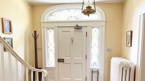 A hallway with a white door, a radiator, and a staircase. - Kilburn Manor 1820 Historical house (Malone)