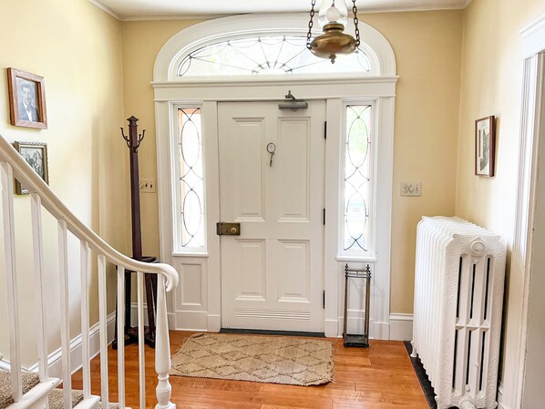 A hallway with a white door, a radiator, and a staircase. - Kilburn Manor 1820 Historical house (Malone)