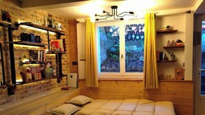 A cozy room with a wooden bed, a brick wall, shelves with books and decorative items, and a window with curtains. - Independent industriel chalet @O&R's (Villejuif)