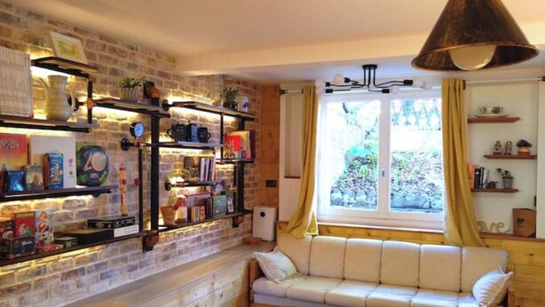 A cozy living room with a brick wall, a white sofa, a wooden table, and shelves with books and decorative items. - Independent industriel chalet @O&R's (Villejuif)