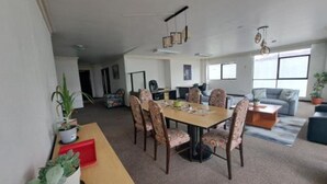 Amplia sala de estar con mesa de comedor, sillas, sofá y mesa de centro. Hay plantas en macetas y un ventanal grande que proporciona luz natural.