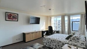Una habitación de hotel con cama, escritorio, silla, televisión y ventana con vistas.