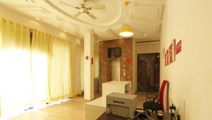 A hotel lobby with a reception desk, a ceiling fan, a television, and a wooden counter with a printer. - OYO Rooms 766 Delhi Airport (New Delhi)