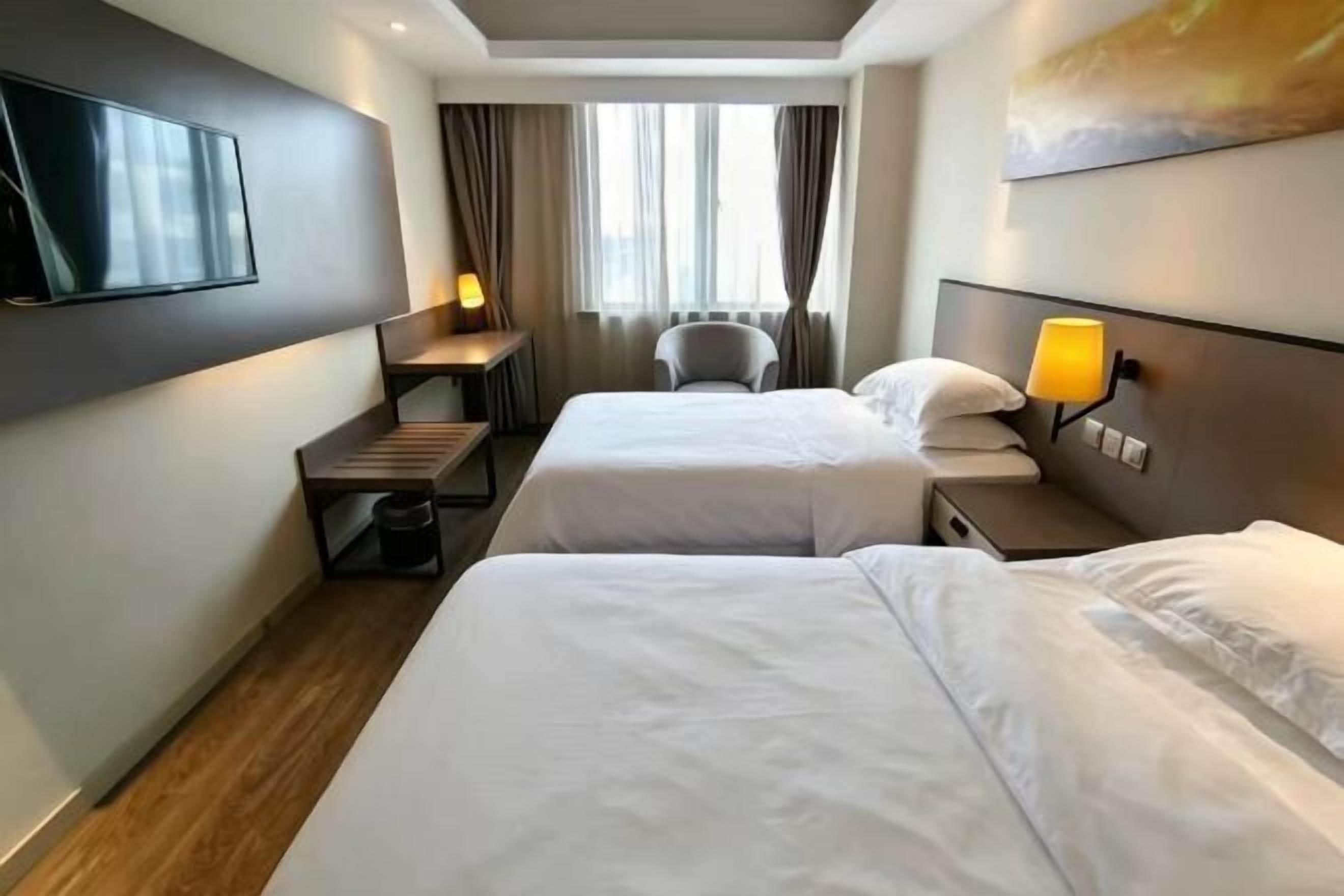 Habitación de hotel con dos camas, un escritorio, una silla, un televisor y una ventana con cortinas.