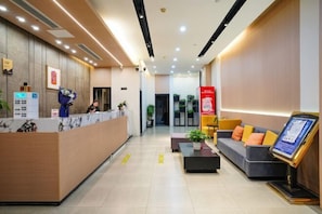 A hotel reception area with a wooden reception desk, a waiting area with a sofa and a coffee table, and a digital information kiosk. - Ripple Hotel (Sihong Renmin Road) (Sihong)