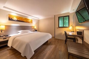 A hotel room with a bed, bedside table, desk, chair, and a TV mounted on the wall.