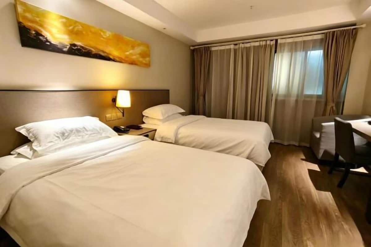 A hotel room with two beds, a desk, a chair, a lamp, and a painting on the wall.