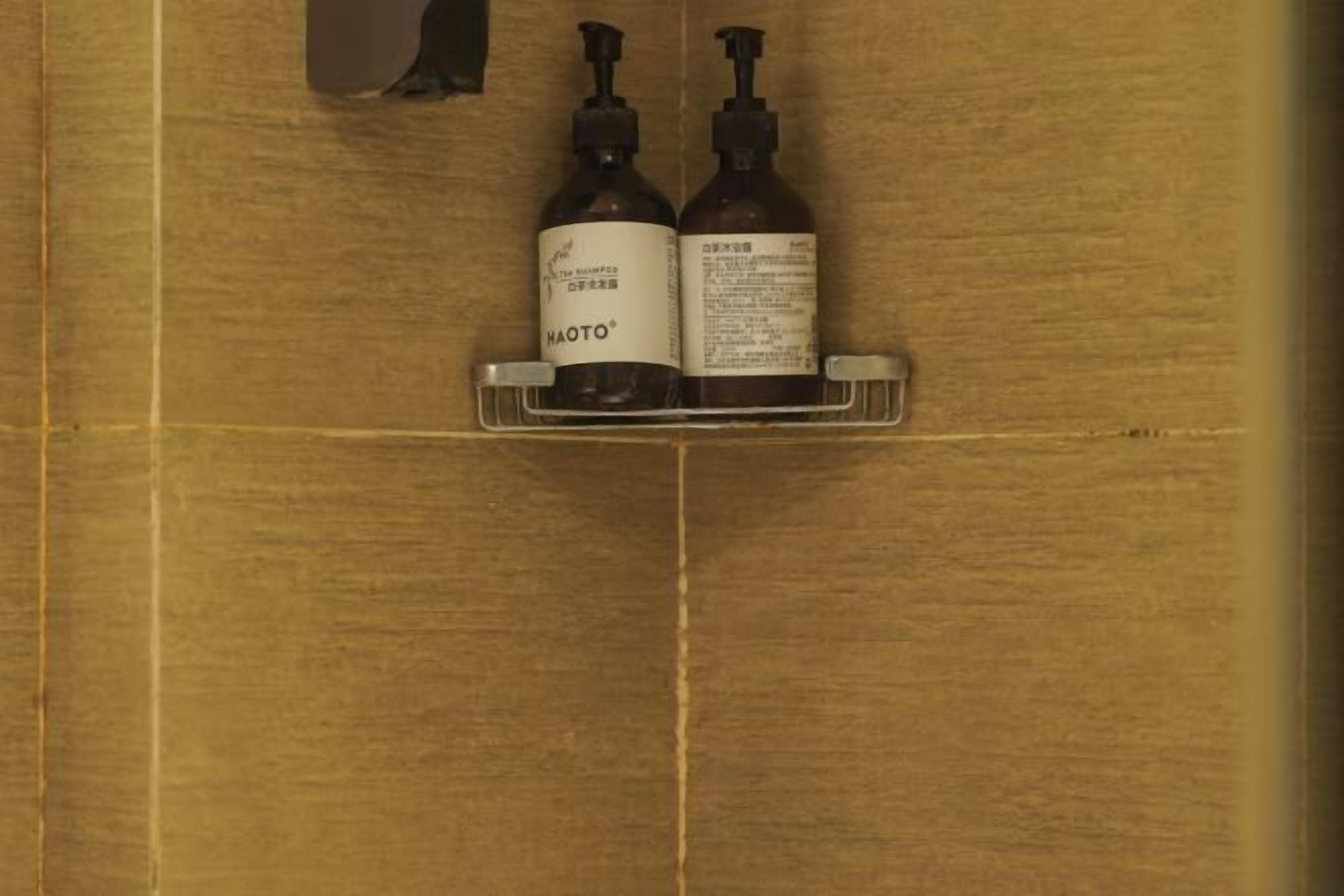 Two bottles of shampoo on a metal shelf in a bathroom with wooden walls.