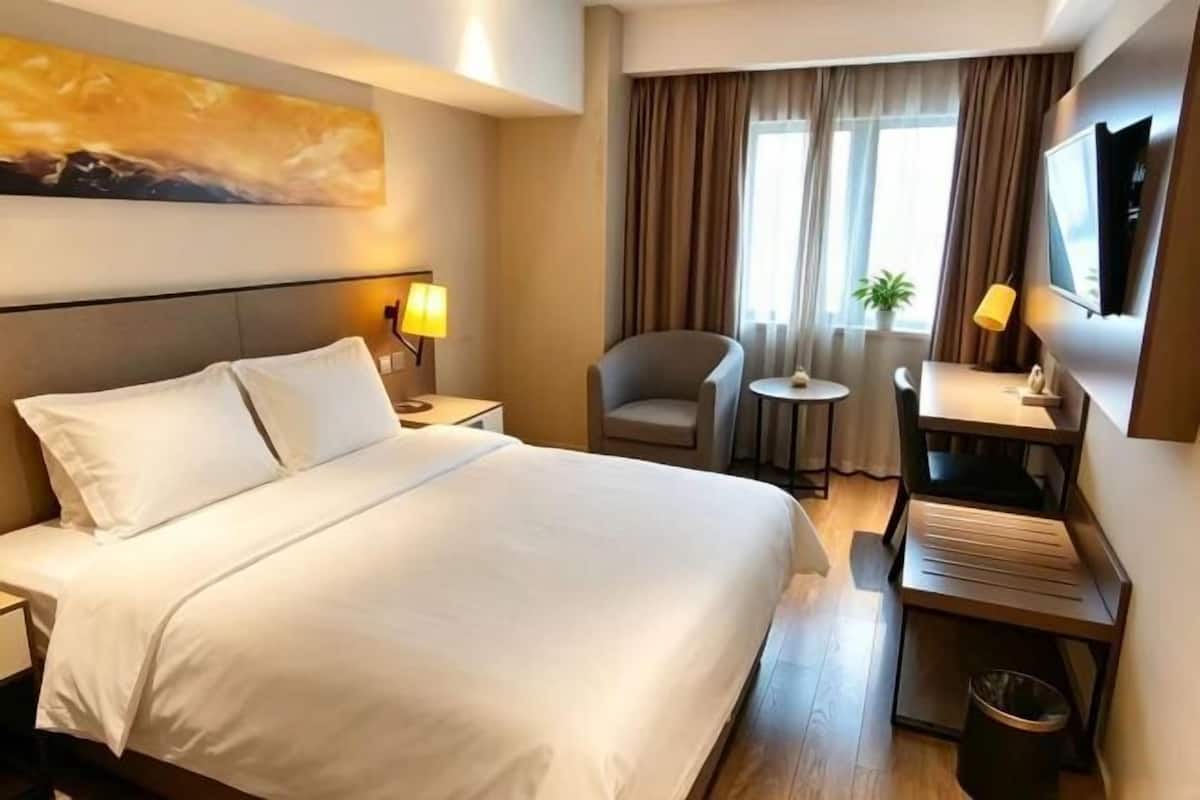 A hotel room with a large bed, a desk, a chair, a TV, and a window with curtains.