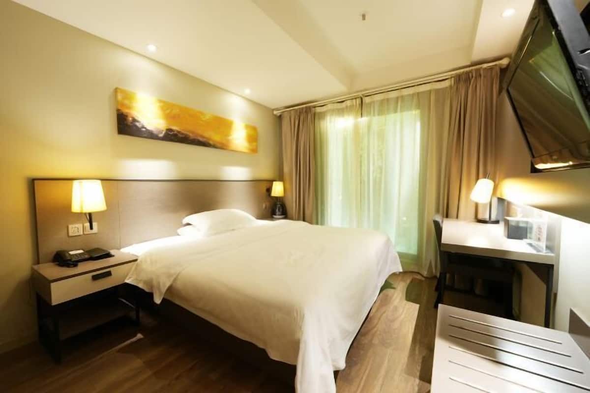 A hotel room with a bed, bedside tables, a desk, a chair, a television, and a painting on the wall.