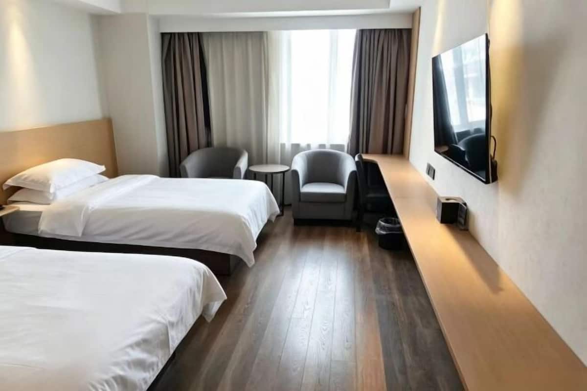 A hotel room with two beds, a desk, a chair, a TV, and a window with curtains.
