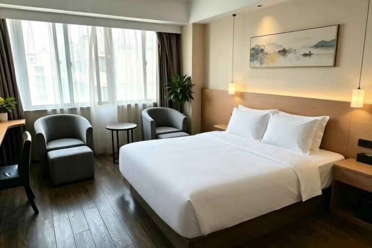 A hotel room with a large bed, two armchairs, a small table, and a painting on the wall.