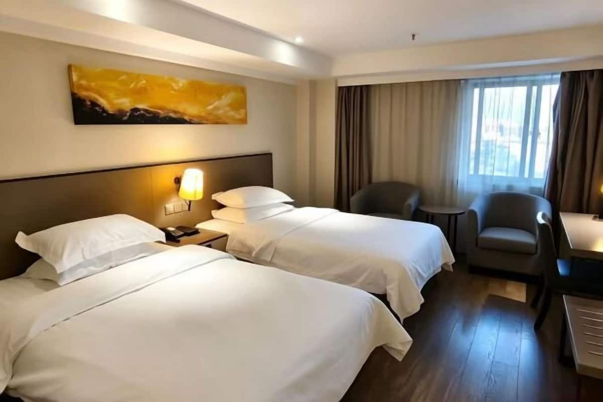 A hotel room with two beds, a desk, a chair, a lamp, and a painting on the wall.