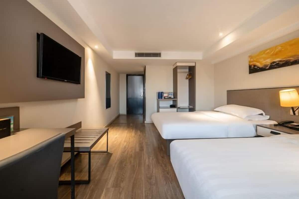 A modern hotel room with a flat-screen TV, a desk, two beds, and a painting on the wall.