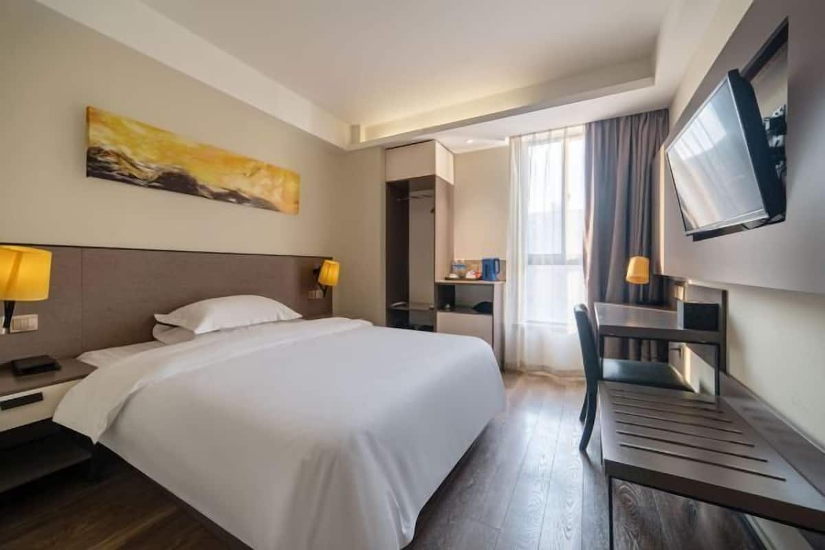 A hotel room with a bed, bedside lamps, a desk, a chair, a TV, and a painting on the wall.