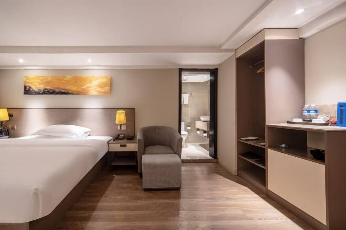 A hotel room with a bed, bedside tables, a chair, a desk, and a wardrobe.